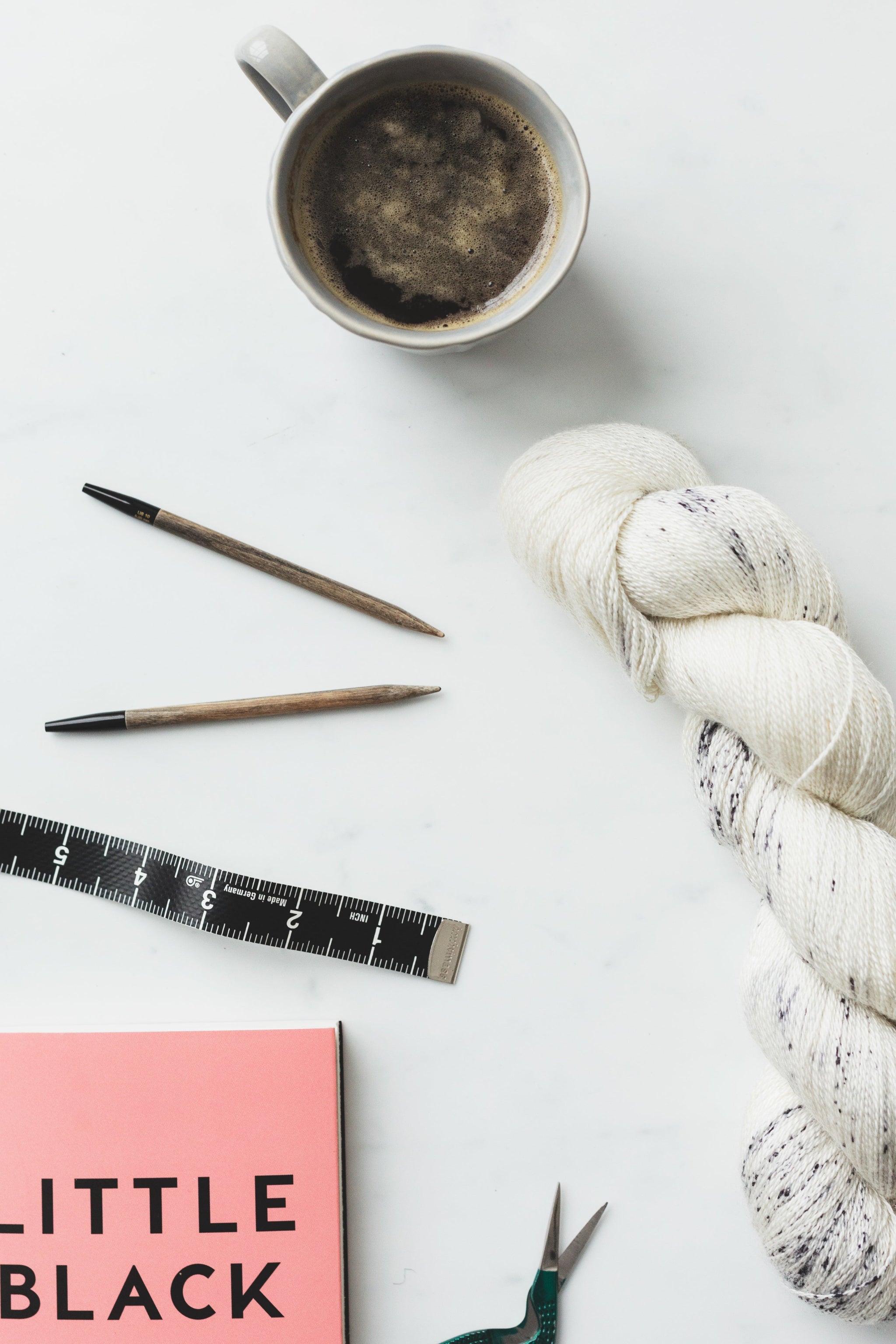 Yarn, knitting needles, and a cup of coffee on a white surface